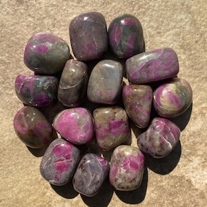 Puede incluir: Una colección de piedras de zoisita rubí rosa y gris pulidas. Las piedras son lisas y pulidas, con una variedad de formas y tamaños.