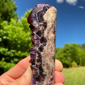 May include: A purple and white amethyst crystal with a natural, rough texture. The crystal is shaped like a tall, thin rectangle and has a pointed top.