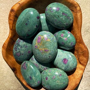 Peut inclure: Un bol en bois rempli de pierres polies de forme ovale. Les pierres sont d'un vert profond, parsemées d'inclusions rouges vibrantes. Le bol lui-même est en bois avec un grain naturel et chaleureux.