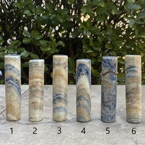 May include: Six polished blue and white banded agate cylinders, numbered 1 through 6. The cylinders are arranged in a row on a light gray surface.