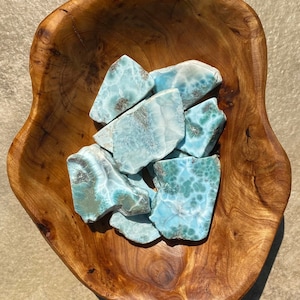 May include: A collection of blue and green ocean jasper stones in a wooden bowl. The stones have a unique, swirling pattern.