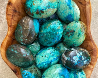 May include: A bowl of tumbled green and blue chrysocolla stones. The stones are smooth and polished, with a variety of patterns and textures.