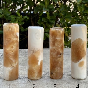May include: Four cylindrical pieces of polished orange calcite, each with a different pattern of white and orange swirls. The pieces are numbered 1 through 4.