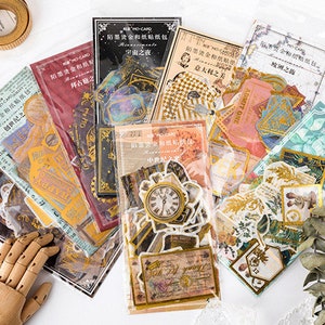 May include: A collection of decorative paper stickers in various designs, including clocks, tickets, and botanical illustrations. The stickers are packaged in clear plastic sleeves, with some featuring gold foil accents and Chinese text. The overall aesthetic is vintage and artistic.