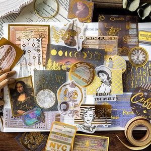 May include: A collection of vintage-style stickers and ephemera with gold foil accents. Includes images of the Mona Lisa, a violin, a clock, and various text elements like "Paris Modio" and "Coffee". The stickers are arranged on a white surface.