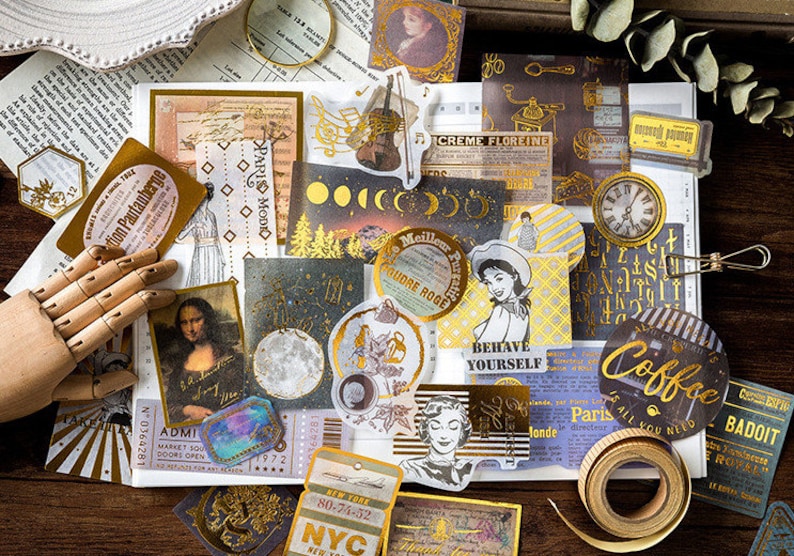 May include: A collection of vintage-style stickers and ephemera with gold foil accents. Includes images of the Mona Lisa, a violin, a clock, and various text elements like "Paris Modio" and "Coffee". The stickers are arranged on a white surface.