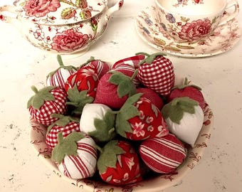 May include: A collection of fabric strawberry ornaments in a patterned bowl, accompanied by a matching lidded tureen and a teacup with saucer. The strawberries feature red, white, and green fabric patterns with felt leaves in various designs.