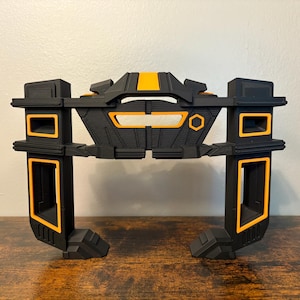 May include: Black and yellow 3D printed stand with two vertical supports and a horizontal top piece. The stand has a geometric design with a hexagonal shape in the center.