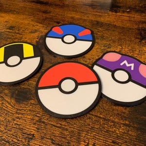 May include: Four round coasters with a white center and a black outline. Each coaster has a different colored ring around the center: red, blue, yellow, and purple. The purple coaster has a letter "M" in the center of the ring.