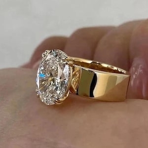 Op de afbeelding: Een gouden ring met een grote, ovaal geslepen diamant. De diamant is gezet in een prong setting en de band is van dik, gepolijst goud. De ring wordt op een hand getoond.