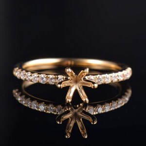 May include: A gold ring with a diamond-studded band and a star-shaped setting. The ring is reflected on a black surface, creating a symmetrical image. The ring is a piece of jewellery.