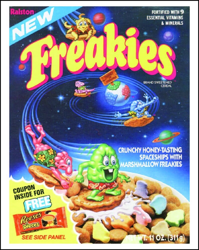 May include: A box of Ralston Freakies cereal featuring a space-themed design with cartoon characters. The box has a coupon for a free package of Reese's Pieces. The cereal is described as "Crunchy Honey-Tasting Spaceships with Marshmallow Freakies" and is fortified with 9 essential vitamins and minerals. The box is 11 ounces (311g).
