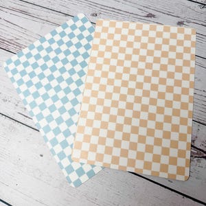 May include: Two rectangular cards with rounded corners. One card features a light blue and white checkered pattern, while the other has a peach and white checkered design. The cards are slightly overlapping, showcasing the contrasting colors and patterns.