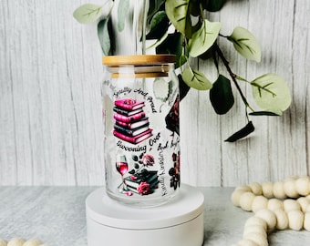 May include: A clear glass tumbler with a bamboo lid and a clear straw. The tumbler features a design with stacked books, a glass of wine, and the words "Smutty and Proud, Swooning Over Kindle Kinkston."