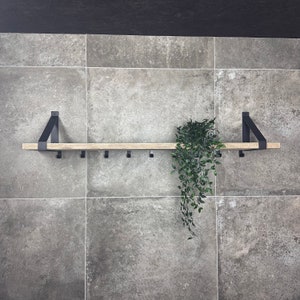 Puede incluir: Una estanter&iacute;a de madera con soportes y ganchos de metal negro, montada en una pared de azulejos grises. Una planta verde cuelga de la estanter&iacute;a.