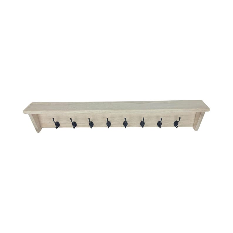 Puede incluir: Estante de madera clara con ocho ganchos de metal negro. El estante tiene un dise&ntilde;o simple y rectangular. Los ganchos est&aacute;n espaciados uniformemente a lo largo del borde inferior, ideales para colgar abrigos, sombreros u otros art&iacute;culos. Mide unos 90 cm de largo.