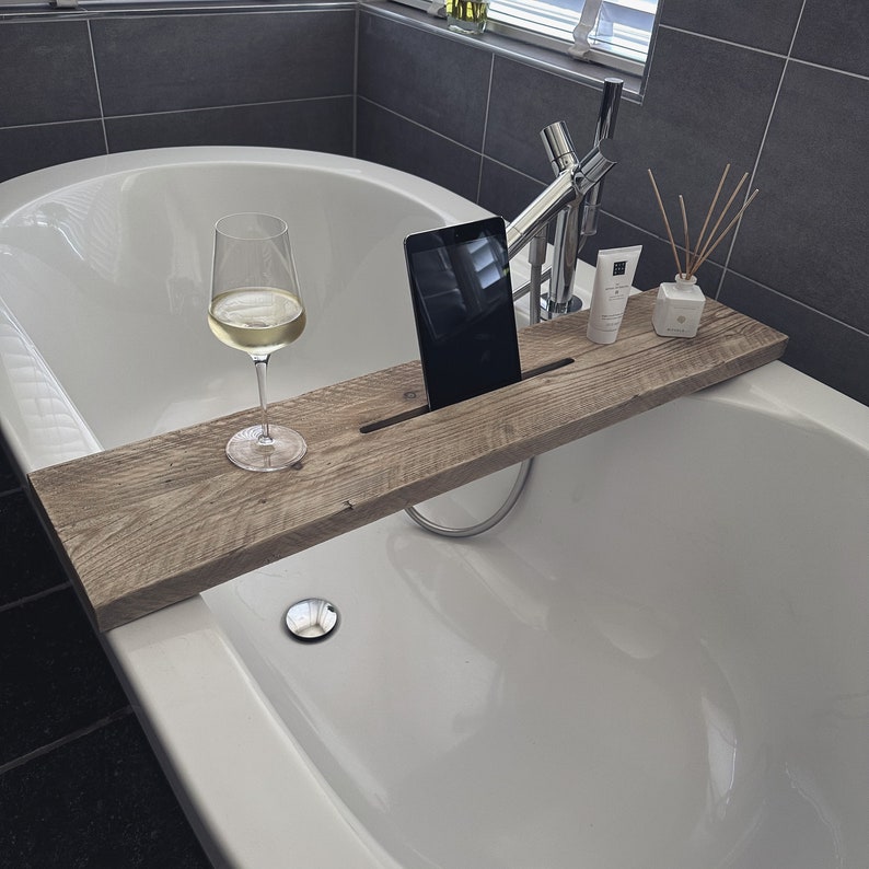 Puede incluir: Una bandeja de ba&ntilde;o de madera con una copa de vino blanco, una tableta y una botella de loci&oacute;n. La bandeja est&aacute; colocada en el borde de una ba&ntilde;era blanca.