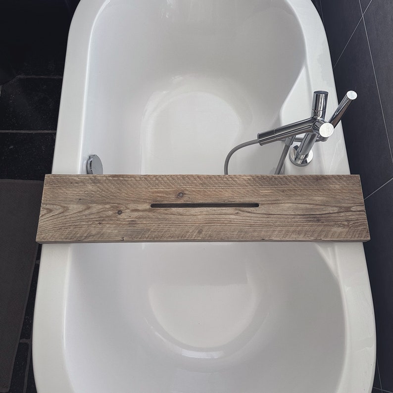Puede incluir: Una ba&ntilde;era blanca con una bandeja de ba&ntilde;o de madera. La bandeja tiene una ranura en el medio y est&aacute; hecha de madera recuperada. La ba&ntilde;era tiene un grifo cromado con una ducha de mano.