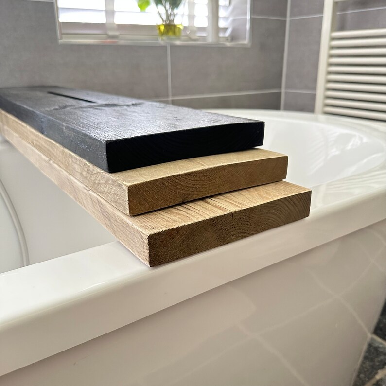 May include: Three wooden bath trays stacked on top of each other. The top tray is black, the middle tray is light brown, and the bottom tray is a darker brown.