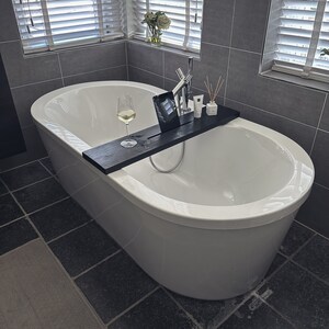 May include: A white bathtub with a wooden tray and a glass of wine. The tray has a tablet, a bottle of lotion, and a bottle of essential oil.