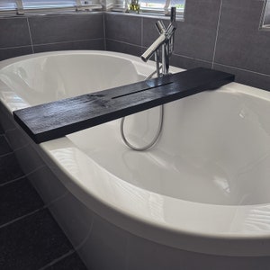 May include: A white bathtub with a black wooden bath tray. The tray is placed across the bathtub and is positioned over the faucet.