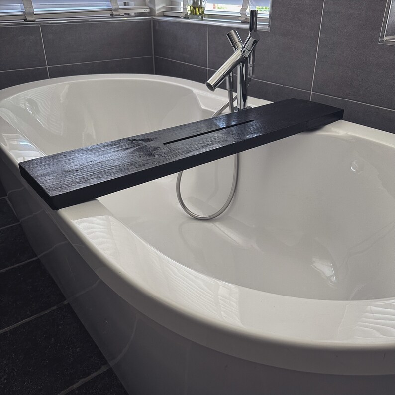 May include: A white bathtub with a black wooden bath tray. The tray is placed across the bathtub and is positioned over the faucet.