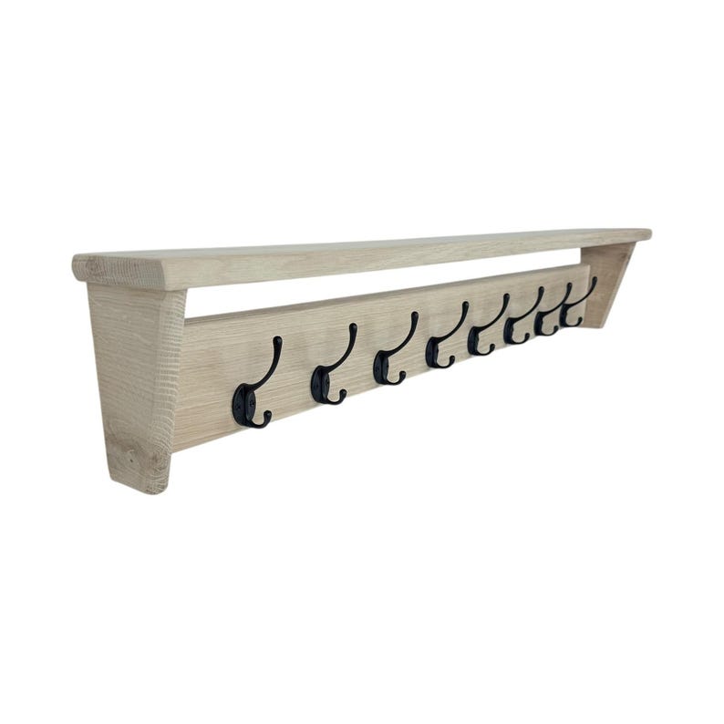 Puede incluir: Un perchero de pared de madera de color claro con una balda y ocho ganchos de metal negro. El perchero est&aacute; hecho de madera de color claro y tiene un dise&ntilde;o simple y minimalista. Los ganchos est&aacute;n espaciados uniformemente.