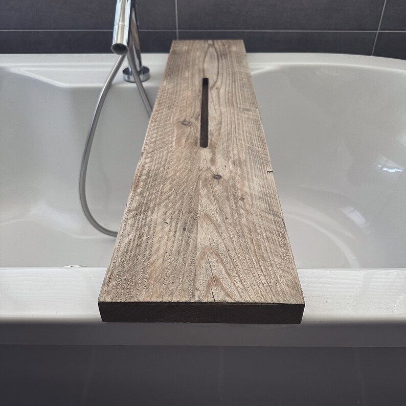 Puede incluir: Una bandeja de ba&ntilde;o de madera con forma rectangular y una ranura en el centro. La bandeja est&aacute; hecha de madera natural de color marr&oacute;n claro y textura rugosa.