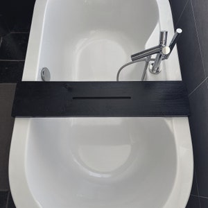 May include: A white bathtub with a black wooden bath tray and a chrome faucet. The tray has a groove in the middle.