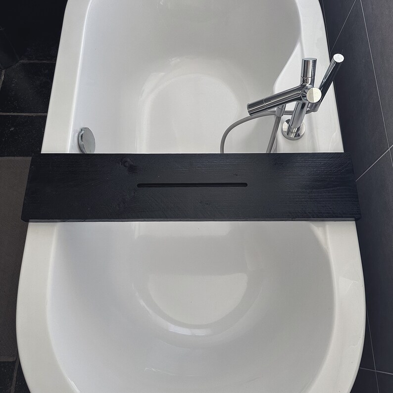 May include: A white bathtub with a black wooden bath tray and a chrome faucet. The tray has a groove in the middle.