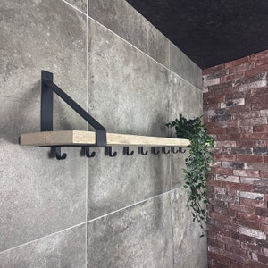 Puede incluir: Una estanter&iacute;a de madera con soportes y ganchos de metal negro montados en una pared de azulejos grises. La estanter&iacute;a est&aacute; decorada con una planta en maceta.