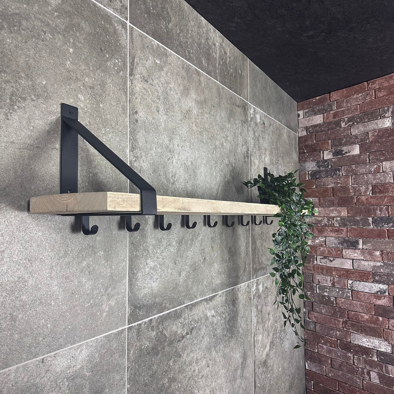 Puede incluir: Una estanter&iacute;a de madera con soportes y ganchos de metal negro montados en una pared de azulejos grises. La estanter&iacute;a est&aacute; decorada con una planta en maceta.