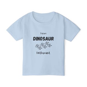 Op de afbeelding: Lichtblauw T-shirt met de tekst "Future Dinosaur Enthusiast" in zwart. Het shirt heeft een dinosaurusvoetprint-afbeelding. Een casual T-shirt met korte mouwen voor kinderen.