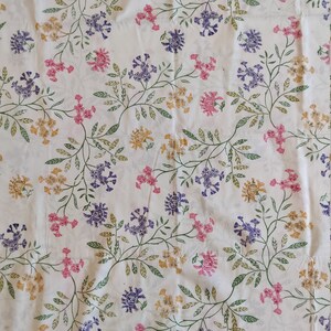 Könnte beinhalten: Weißer Stoff mit einem sich wiederholenden Muster aus grünen Blättern und kleinen lila, rosa und gelben Blüten.