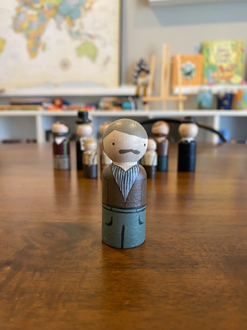 May include: A hand-painted wooden peg doll with a brown shirt, green pants, and a gray mustache. The doll is standing on a wooden surface.