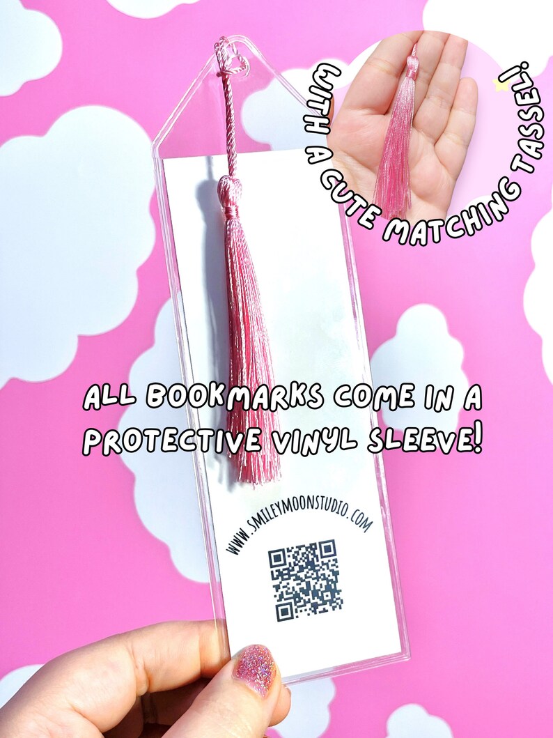 Op de afbeelding: Een transparante acryl bladwijzer met een roze kwast. De bladwijzer heeft een witte achtergrond met een QR-code en de tekst "WWW.SMILEYMOONSTUDIO.COM". De tekst "ALL BOOKMARKS COME IN A PROTECTIVE VINYL SLEEVE!" is op de bladwijzer gedrukt. De bladwijzer wordt in een hand met roze nagellak gehouden.