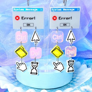 May include: A pair of dangle earrings featuring a white rectangular charm with the text System Message and Error! with a red X icon. Below are smaller charms including a pink Ctrl square, a yellow folder, a white cursor, a pink Del square, and an hourglass.