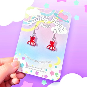 May include: Red octopus shaped acrylic earrings on a white card with the text "Smiley Moon Studio" and "Handmade Acrylic Jewelry & More". The card has a pink heart with a planet around it and a yellow moon.