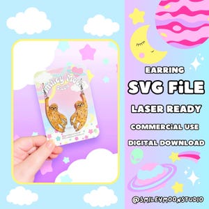 May include: A pair of sloth-shaped earrings on a white card with the text "Smiley Moon Studio". The earrings are made of a light brown material and have a glossy finish. The card is surrounded by a pink and blue background with stars and clouds.