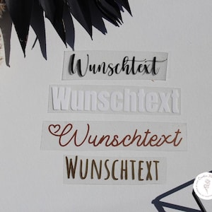 Könnte beinhalten: Vier rechteckige Aufkleber mit dem Wort "Wunschtext" in verschiedenen Schriftarten und Farben. Die Farben umfassen Schwarz, Weiß und Rotbraun. Die Aufkleber befinden sich auf einem weißen Hintergrund mit dekorativen Elementen.