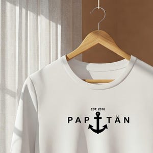 May include: White long-sleeve t-shirt with a black anchor graphic and the text "EST. 2016 PAPTÄN".