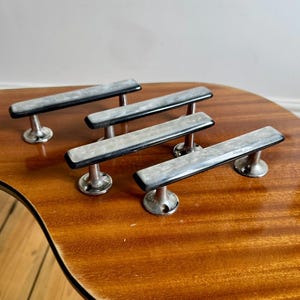 May include: Five vintage cabinet pulls with a rectangular, marbled design in shades of grey and black. The pulls are mounted on a chrome base. The pulls are displayed on a wooden surface.