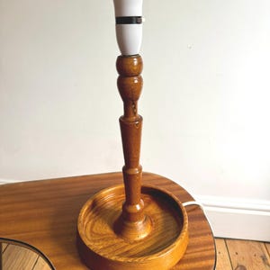 May include: A vintage wooden table lamp with a white lampshade and a dark brown wooden base. The lamp is on a wooden side table with a round tray-like base. The lamp's design is classic and elegant.