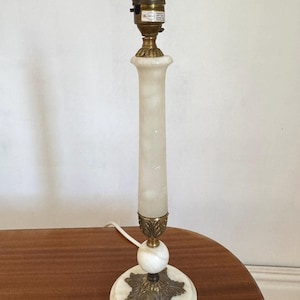 May include: A vintage table lamp with a white marble base and a cylindrical alabaster body. The lamp features brass accents and a standard light bulb socket. The lamp is approximately 38 cm tall.
