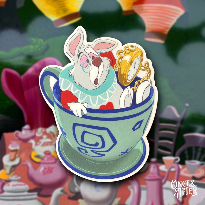 Op de afbeelding: Het Witte Konijn uit Alice in Wonderland zit in een theekopje met een zakhorloge. Het theekopje is blauw en wit met een swirl-ontwerp. Het konijn draagt een vest en een strikje.