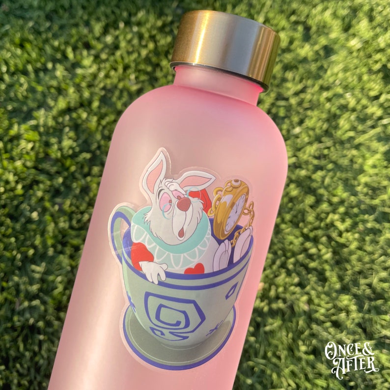 Op de afbeelding: Een roze waterfles met een sticker van een wit konijn. Het konijn draagt een vest en houdt een zakhorloge vast. De sticker is op een lichtroze achtergrond.