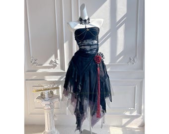 May include: A black and white strapless dress with a lace overlay and a red rose accent. The dress has a layered skirt with a sheer overlay. The dress is on a mannequin in a white room.