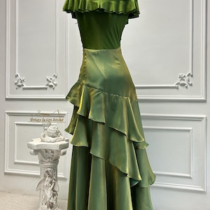 May include: A green off-the-shoulder dress with a ruffled neckline and tiered skirt. The dress is displayed on a mannequin. The text "Vintage Design Amour" is visible on a sign in the background.
