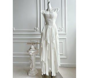 Op de afbeelding: Een witte off-the-shoulder jurk met een gerimpeld lijfje en gelaagde rok. De jurk wordt getoond op een mannequin, die het vloeiende, romantische ontwerp laat zien. Een delicate ketting siert de halslijn. Vintage design.