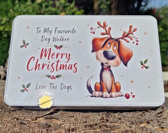 May include: A rectangular white metal tin featuring a cartoon dog wearing reindeer antlers. The text reads: To My Favourite Dog Walker, Merry Christmas, Love The Dogs. The design includes holly berries and small stars on a white background.